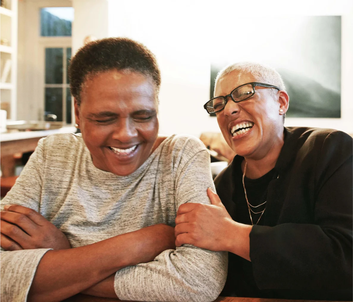 Two friends laughing expressively, one friend holding the other's arm